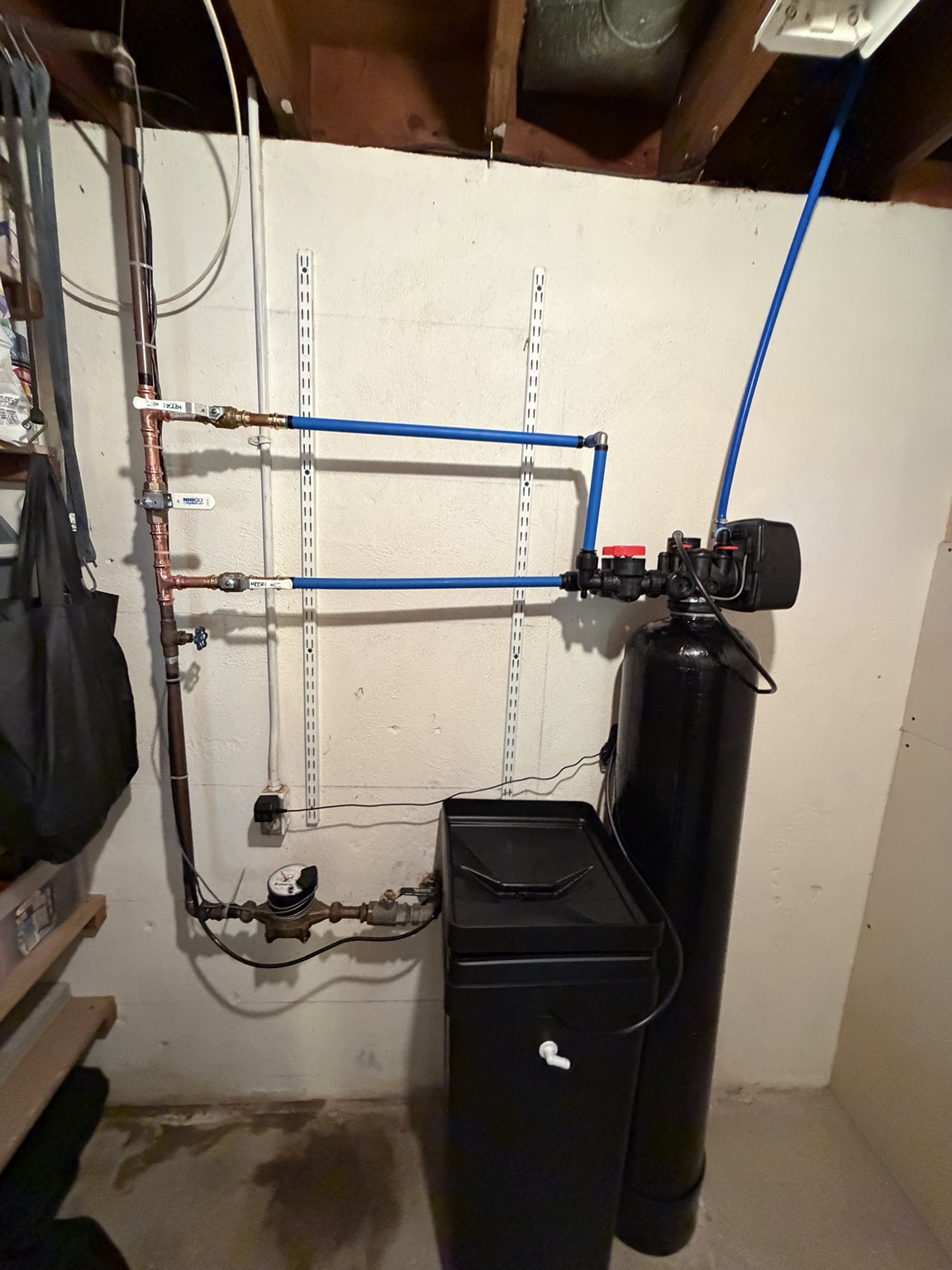 Black water softener for hard town water with a digital control head and separate brine tank connected to copper and blue piping.